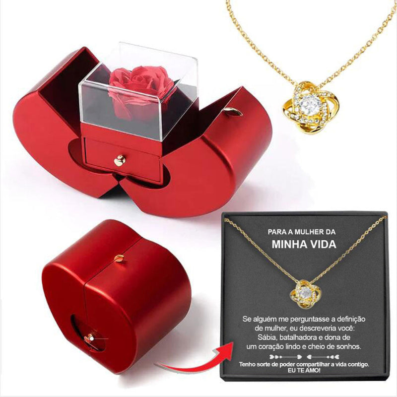 Red jewelry box with a rose, gold necklace with heart pendant, and black card on a white background