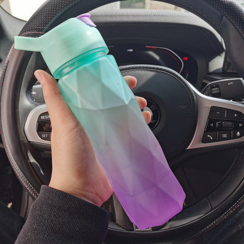 Hand holding a gradient green to purple water bottle in front of a car dashboard.