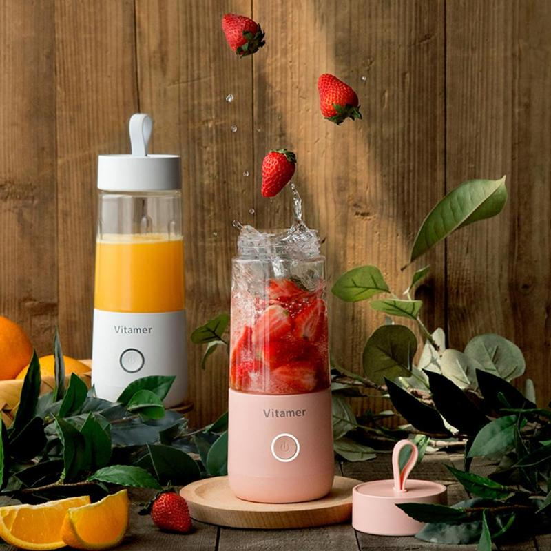 Pink Vitamer blender with strawberries and orange juice on a wooden surface with plants.